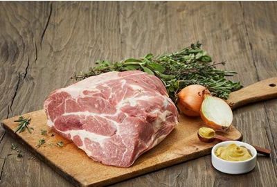 Roher Schweinehals auf einem Holzbrett mit Zwiebel, Senf und frischen Kräutern.