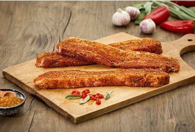 Gewürzte Grillbauchscheiben der Metzgerei Fritsch liegen auf einem Holzbrett, daneben frischer Knoblauch, Chilischoten, Kräuter und eine Schale mit Gewürzmischung – angerichtet auf einem rustikalen Holztisch.
