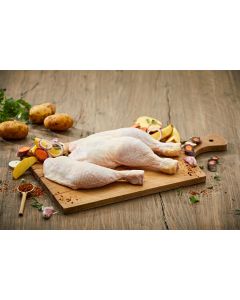 Zwei frisch zubereitete Bauernhähnchenschenkel auf einem Holzbrett, umgeben von Kartoffeln, Karotten, Zwiebeln und Knoblauch. Bauernhähnchen kaufen bei Metzgerei Fritsch.
