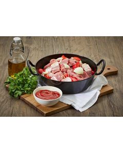 Schaschlikpfanne im Schmortopf: Schweinefleisch, Paprika, Zwiebeln und Speck, dekoriert mit Ketchup und frischen Kräutern auf einem rustikalen Holzbrett.