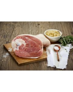 Gepökelte Surhaxe von Metzgerei Fritsch auf einem Holzbrett, serviert mit Salz aus Holz und einem Schälchen Kartoffelsalat. Das zarte Fleischstück ist umgeben von Kräutern und einem Stofftuch, ideal für festliche Gerichte.