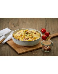 Bayerischer Kartoffelsalat – mit Speck in heller Keramikschale auf Holzbrett, grob geschnittene Kartoffeln vermengt mit Speckwürfeln und frischer Petersilie, neben kleinen Tomaten und Speckglas.