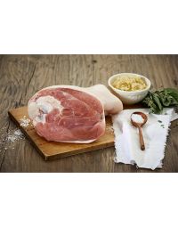 Gepökelte Surhaxe von Metzgerei Fritsch auf einem Holzbrett, serviert mit Salz aus Holz und einem Schälchen Kartoffelsalat. Das zarte Fleischstück ist umgeben von Kräutern und einem Stofftuch, ideal für festliche Gerichte.