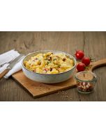 Bayerischer Kartoffelsalat – mit Speck in heller Keramikschale auf Holzbrett, grob geschnittene Kartoffeln vermengt mit Speckwürfeln und frischer Petersilie, neben kleinen Tomaten und Speckglas.