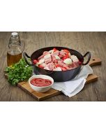 Schaschlikpfanne im Schmortopf: Schweinefleisch, Paprika, Zwiebeln und Speck, dekoriert mit Ketchup und frischen Kräutern auf einem rustikalen Holzbrett.